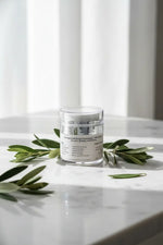 Skincare jar with olive leaves on a marble surface