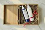Two skincare products in a wooden box with a red ribbon on a marble surface