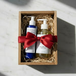 Two bottles with a red ribbon in a wooden box on a light surface