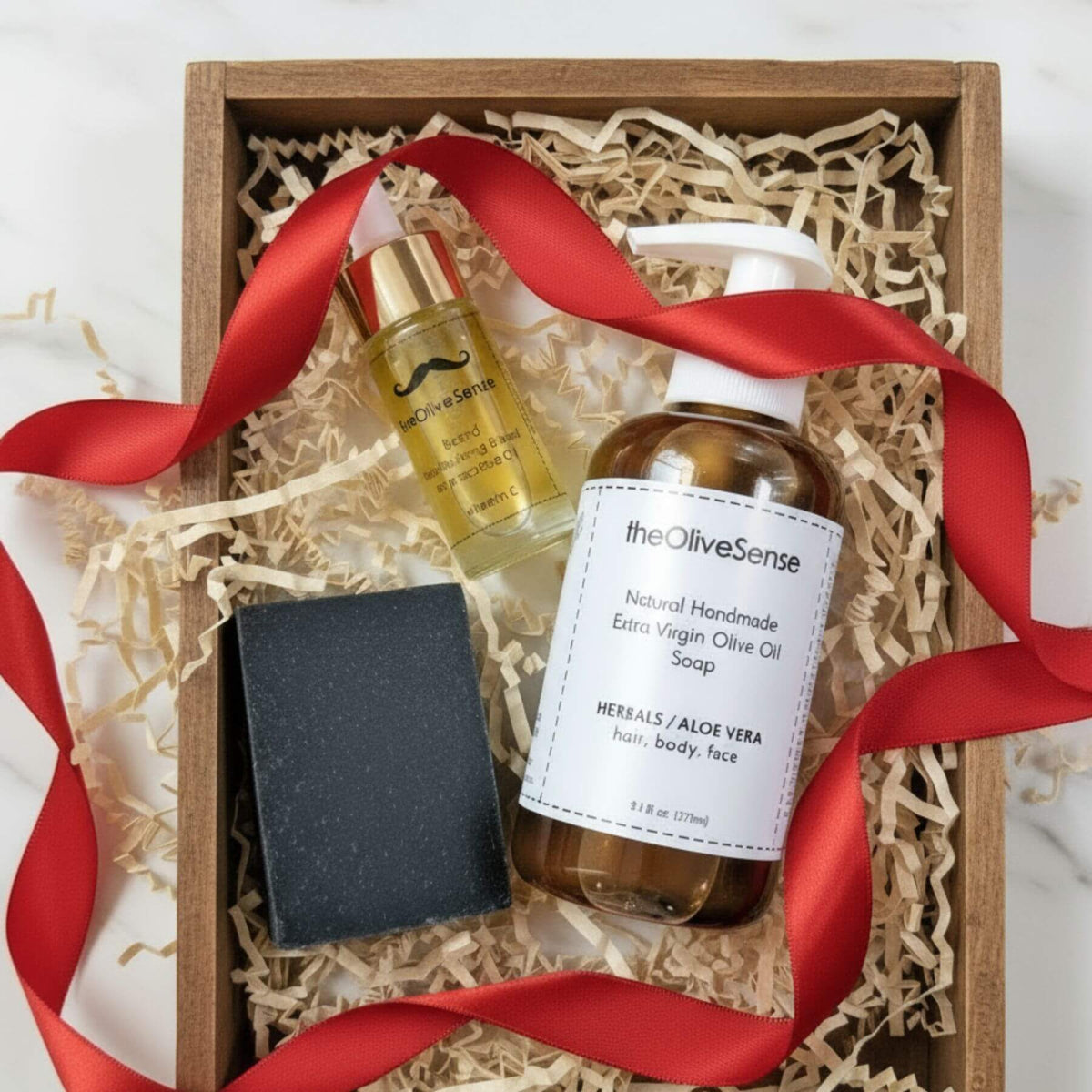 Gift set with olive oil products and a red ribbon in a wooden box.