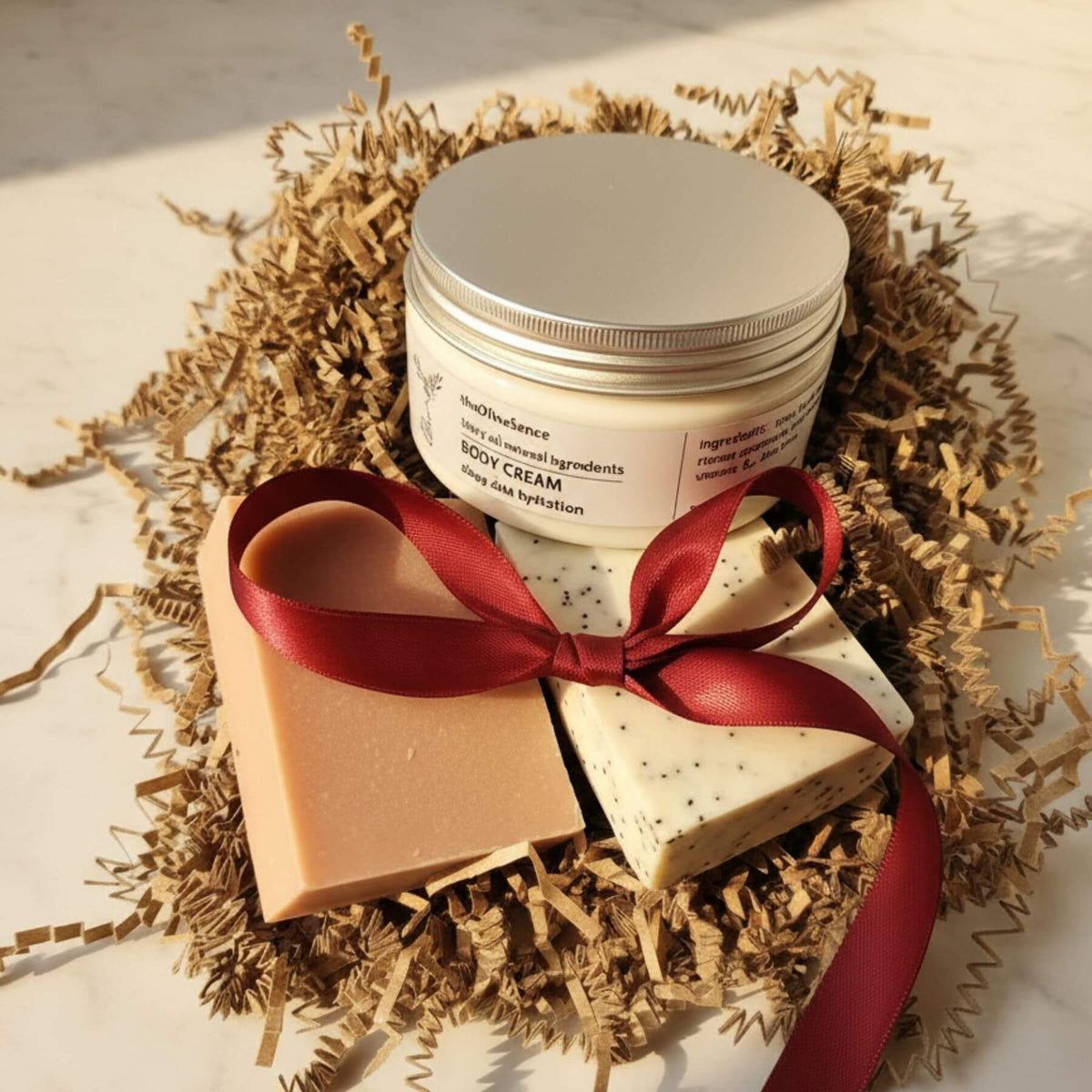 Jar of body cream, heart-shaped soap, and square soap with a red ribbon on a bed of straw.