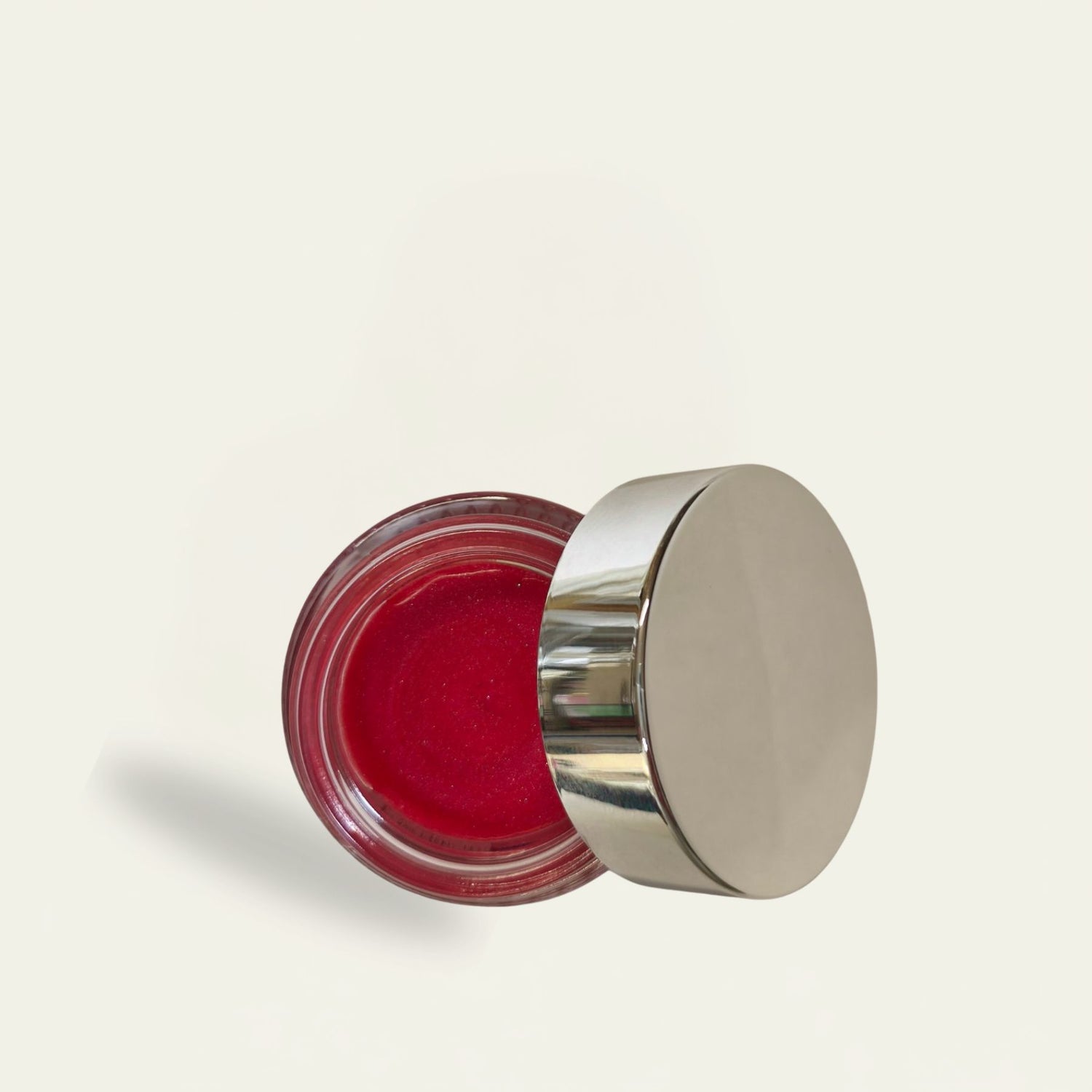 Open jar of red cream with a silver lid on a light beige background