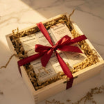 Gift box with a red ribbon containing products from The Olive Sense on a marble surface.