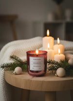 Candle with a label on a wooden table surrounded by Christmas decorations.
