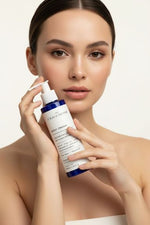 A woman holding a bottle of theOliveSense Body Cream against a clean, light beige background.